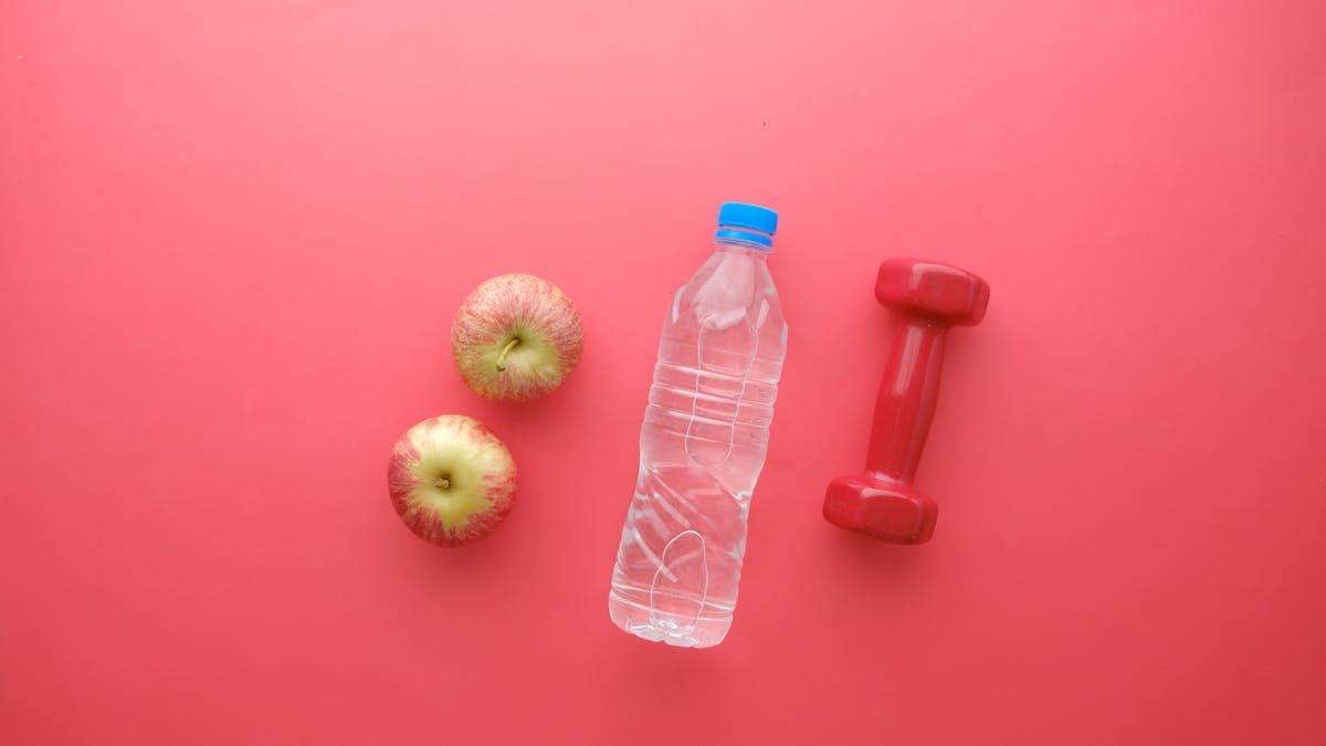 Top view of water bottle, apples, and dumbbell on bright red background. Perfect for fitness and wellness themes.