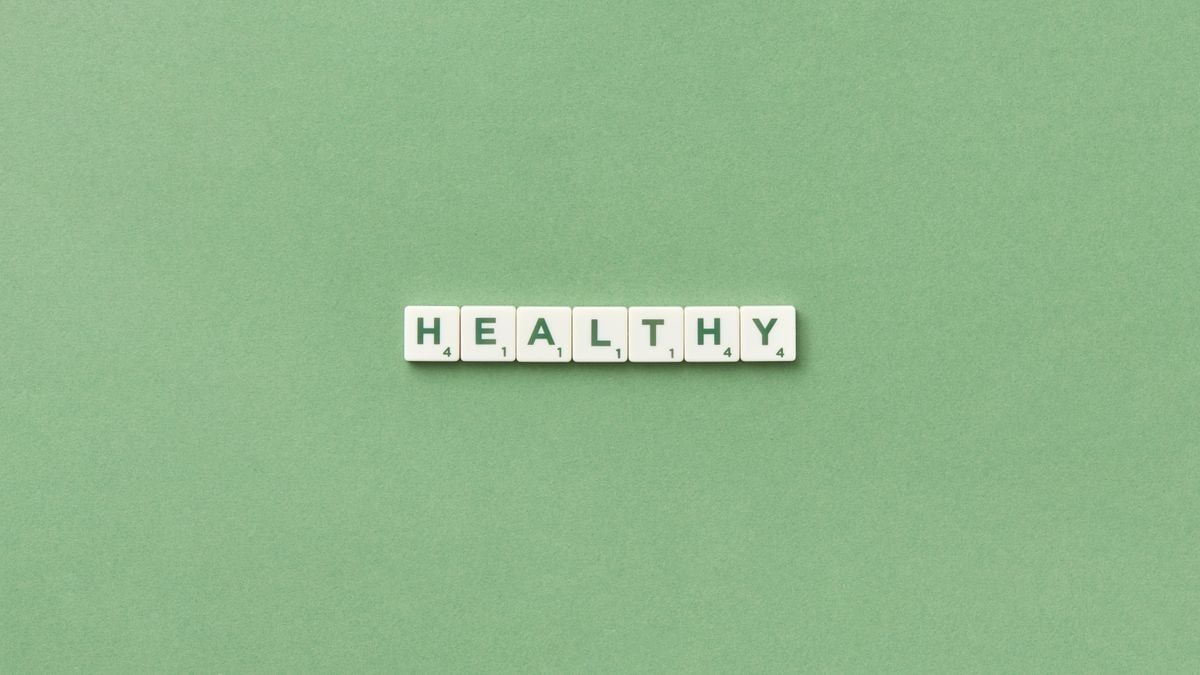 Scrabble tiles spelling the word 'healthy' on a light green background, top view.